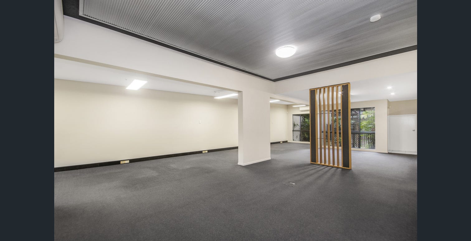 Empty open plan commercial office interior with dark carpet, a timber slat room divider and black framed windows looking out to greenery.