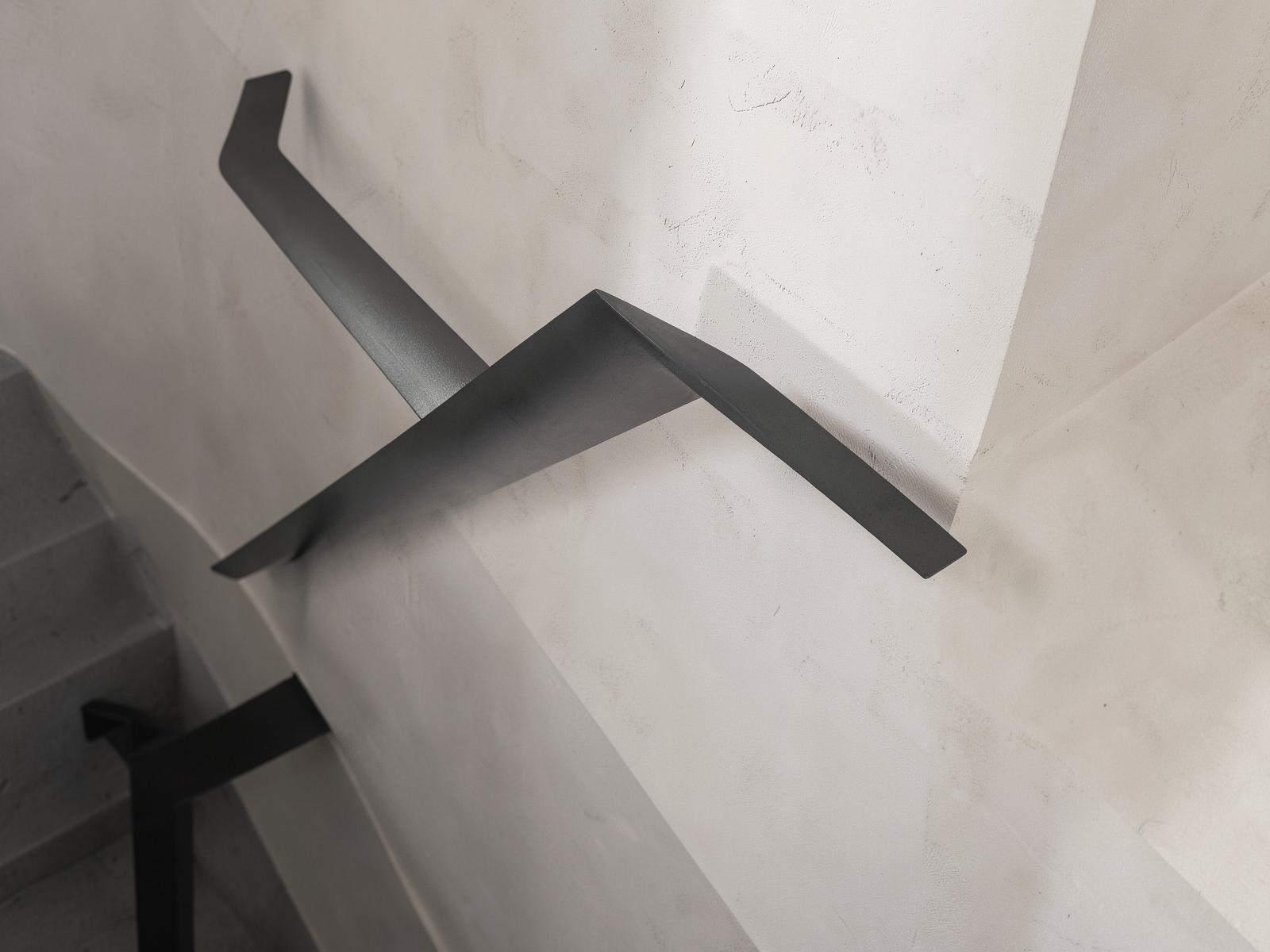 Dark steel handrail against a pale rendered commercial stairwell wall.