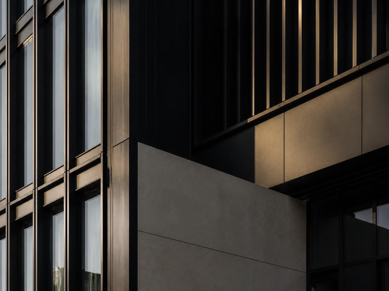 Raking light across a dark steel and glass commercial facade, showing sharp vertical mullions and precast panels.