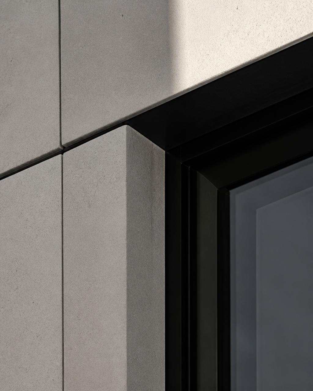 Close detail of a commercial building edge where a precast concrete panel meets a dark steel glazing reveal in raking light.