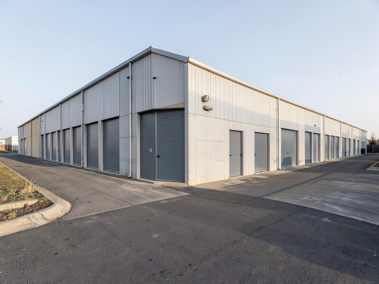 A row of industrial warehouse roller doors along a service road.